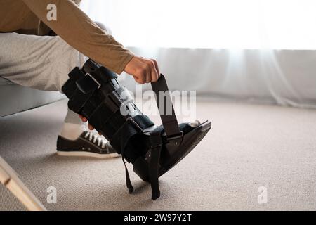 Close-up of a man putting walking brace to his leg sitting on sofa at home Stock Photo
