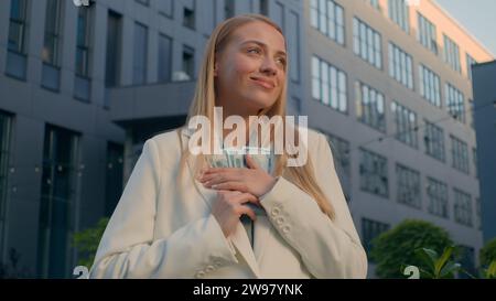 Happy smiling rich caucasian business woman girl businesswoman female winner manager entrepreneur holding cash outdoors near office building waving Stock Photo