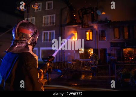 Firefighter spraying water on burning house at night, Haute-Savoie, France Stock Photo