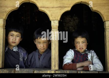 Three boys look out a window in Paro, Bhutan. Stock Photo