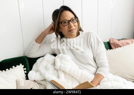 Woman wearing glasses, holidng a book while sitting on couch Stock Photo