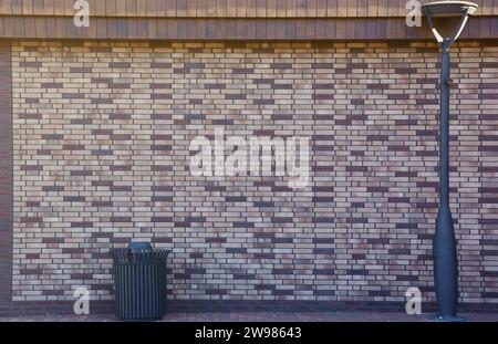 Dark brick wall pattern with chaotic masonry order. Background texture modern stone wall with lamp post and street trash can Stock Photo