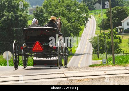 Ronks, Pennsylvania, July 23, 2023 - A Rear View of an Amish Couple in an Open Horse and Buggy, Heading Down a Rural Road on a Sunny Summer Day Stock Photo