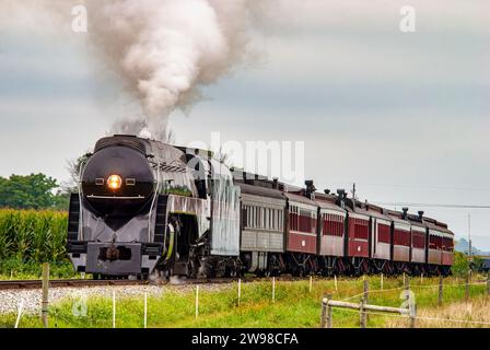 A vintage steam locomotive is chugging along a railway track, emitting plumes of thick smoke Stock Photo