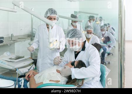 dentistry student in a practical class at college, with the patient with his mouth open and another student helping Stock Photo