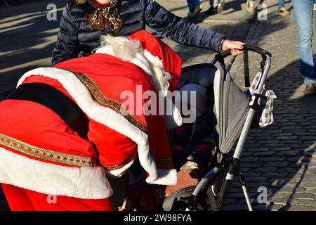 Person dressed as Santa Claus talking to a child in a stroller at the Brussels christmas market on a sunny winter day Stock Photo