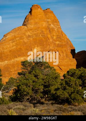 A sun setting at a desert landscape, with a large rock formation in the background Stock Photo