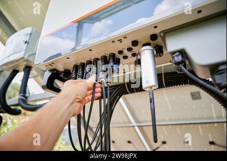 Professional worker connecting wires to solar inverter. Pov of configuring inverter. Male worker turning on PV battery. Stock Photo