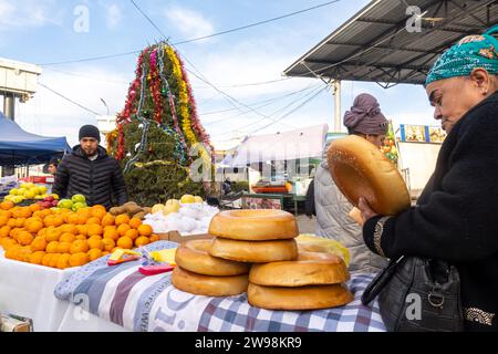 Uzbek woman buying traditional Uzbek round bread at Siyob or Siob Bazaar  stalls with a Christmas tree Samarkand Uzbekistan Stock Photo