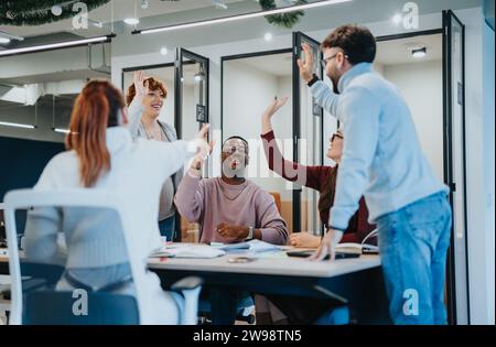 Multicultural group of businesspeople celebrating successful work completion in office. They are giving high five each other. Stock Photo
