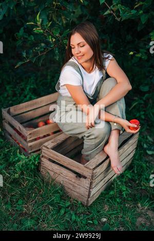 Woman gardener with red juicy apple from tree in own home countryside orchard Stock Photo