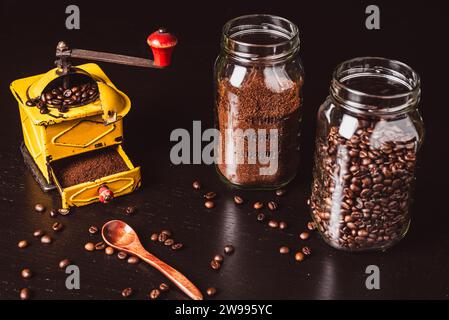 Old coffee grinder next to a wooden spoon and two jars with coffee beans and grounds. Stock Photo