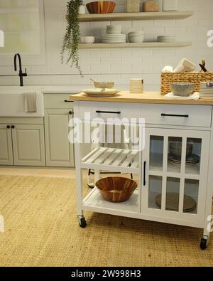 This modern kitchen features white cabinets and wooden shelving for storing cooking and kitchen supplies Stock Photo