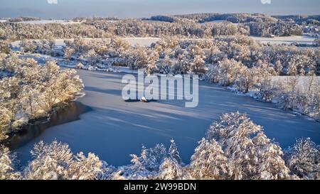 An aerial view of snow-covered trees surrounding a river in the middle of a forest. Stock Photo