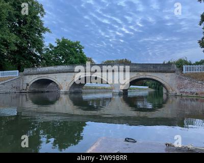 A stone bridge extending across a tranquil body of water, surrounded by lush trees Stock Photo