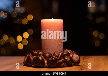 Christmas candle with ring of chestnuts on brown tabel and christmas tree in background bokeh with blurred lights Stock Photo