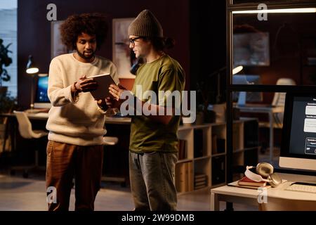 Two young intercultural AI coworkers looking at tablet screen during discussion of new software or while creating new one Stock Photo