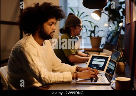 Young serious businessman looking at laptop screen and typing on keyboard while sitting by workplace and working over new project Stock Photo