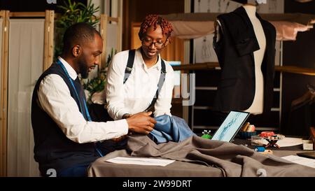 Couturiers team choosing fabric to craft tailored clothes, working in atelier to manufacture fashion items for clothing line. Two tailors picking material, handcraft process. Tripod shot. Stock Photo