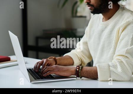 Cropped shot of young bearded male designer or entrepreneur typing on laptop keyboard while working with online data by workplace Stock Photo
