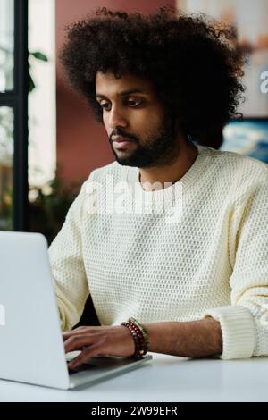 Young serious man typing on laptop keyboard and looking at screen with online information while organizing work or carrying out task Stock Photo