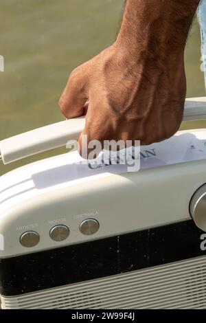 A close-up of a hand holding a white, vintage-style caravan radio. Stock Photo