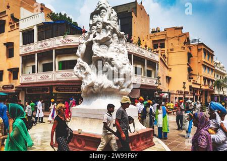 A crowd of people gathered around an ornate statue in the middle of a street of Amritsar Stock Photo