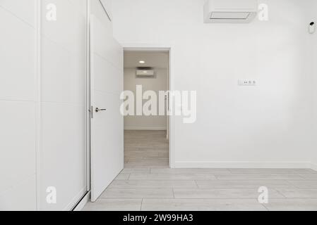 A room in an empty loft-style home with built-in wardrobes with white sliding doors, light wooden floors and air conditioners hanging high on the wall Stock Photo