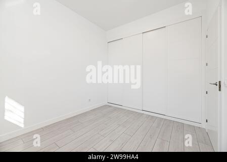 An empty room with built-in wardrobes with white sliding doors along one wall and white wooden carpentry Stock Photo
