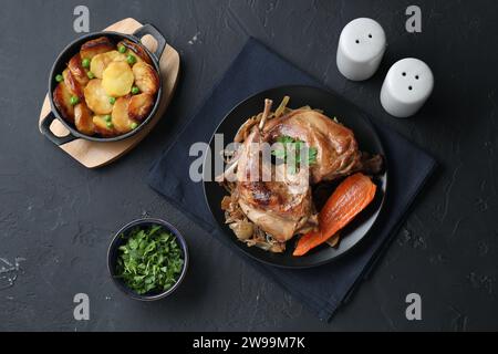 Tasty cooked rabbit meat with vegetables and potato served on black table, flat lay Stock Photo
