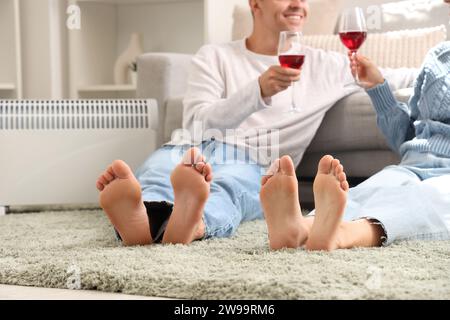 Barefoot young couple with wine warming near radiator at home, closeup Stock Photo