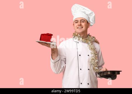 Portrait of young male chef with Christmas tinsel, gift box and baking form on pink background Stock Photo