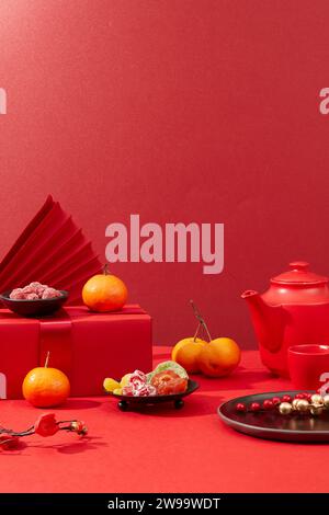 A tea set, jam, salted dried fruit, tangerines, red gift boxes and paper fans are arranged on a background filled with red. Tet decoration with front Stock Photo