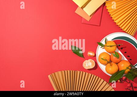 On a bright red background, paper fans, fruit dish and lucky money envelopes are decorated on the right side of the frame. Space on the left for text Stock Photo