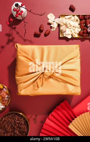 Yellow silk-wrapped gift box, plate of salted dried fruit, jujube, melon seeds, and paper fans arranged on a red background, capturing the essence of Stock Photo
