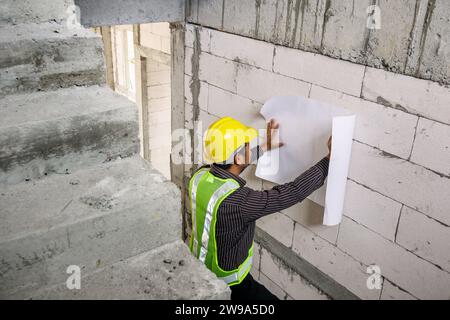 young professional engineer worker in protective helmet working at house building construction site with blueprint Stock Photo