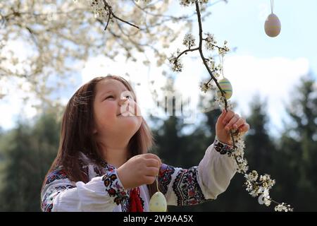 Pretty ukrainian girl wearing vyshyvanka decorating the tree with easter eggs. happy family celebrating easter. Stock Photo