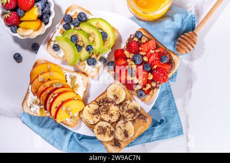 Fruit berry sandwiches. Various toasts with peanut butter, cream cheese, chocolate spread with summer berries and fruits - strawberry, banana, peach, Stock Photo