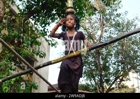 In a street performance or tamasha, a young Indian girl walks a tightrope, with the added difficulty of balancing vessels on her head; Mumbai, India Stock Photo