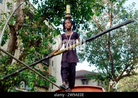 In a street performance or tamasha, a young Indian girl walks a tightrope, with the added difficulty of balancing vessels on her head; Mumbai, India Stock Photo