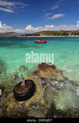 176 Mooring made of an old tire at Rilinda beach, red outboard boat on the background, Ksamil village. Sarande-Albania. Stock Photo