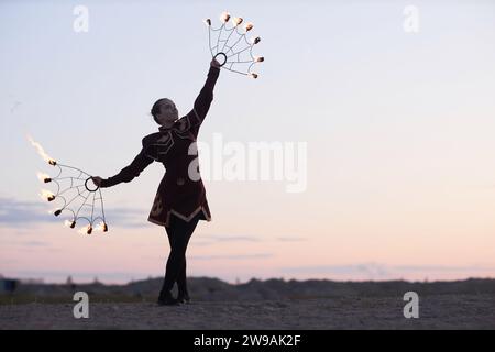 Full length portrait of female fire show performer wearing costume while dancing outdoors in nature, copy space  Stock Photo