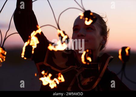 Close up portrait of smiling young woman dancing with flaming fans enjoying performing in fire show Stock Photo