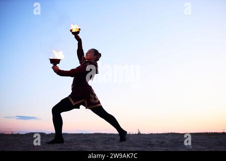 Wide angle view at young woman dancing with flaming bowls performing in fire show on beach outdoors, copy space Stock Photo