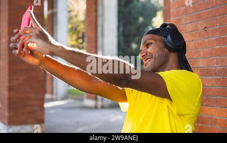 Black guy smiling with headphones while taking a selfie on the street, copy space Stock Photo