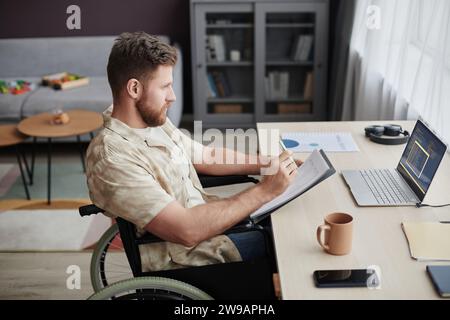 Side view portrait of bearded man with disability designing mobile app while working from home Stock Photo