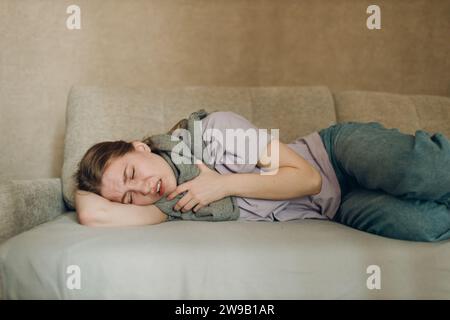 Young woman wearing scarf has flu ill sick disease cold at home indoor lying on sofa Stock Photo