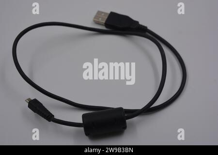 Computer equipment, a long, black micro USB cable from a digital camera to a regular computer, which is located on a white plastic background. Stock Photo
