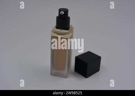 Beautiful, stylish women's cosmetics, very cool glass bottle with foundation, brown cream and matte black square black cap placed on a white plastic. Stock Photo
