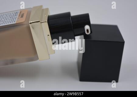 Beautiful, stylish women's cosmetics, very cool glass bottle with foundation, brown cream and matte black square black cap placed on a white plastic. Stock Photo